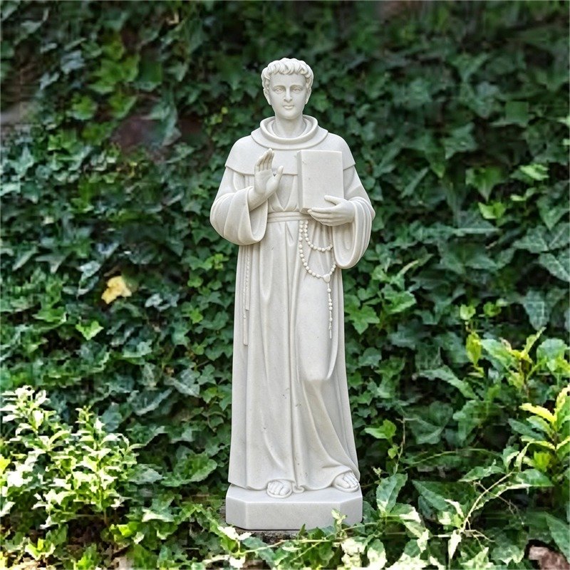 A tall white marble statue of Saint Thomas Aquinas, dressed in a Dominican habit, holding a book in one hand and raising the other in blessing