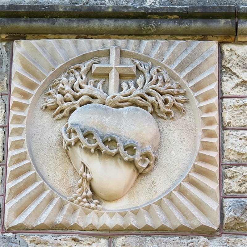 Close-up stone relief carving of the Sacred Heart of Jesus, featuring crown of thorns, cross, and vine details, at the heritage-listed Sacred Heart Church in Highgate, Western Australia