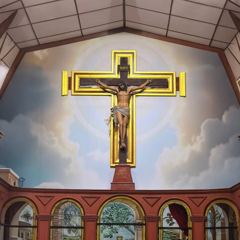 Handmade resin Jesus Christ crucifix displayed on church wall, golden framed cross with stained glass below.