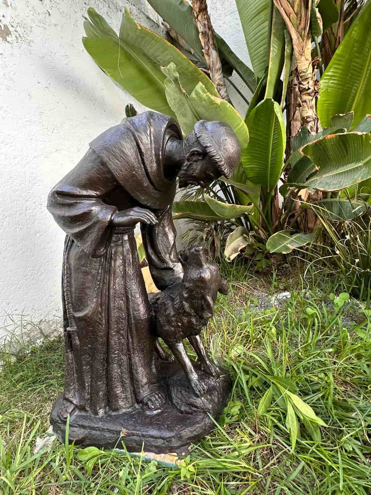 Bronze St. Francis of Assisi statue bending down to pet a wolf in a tropical garden in Mexico