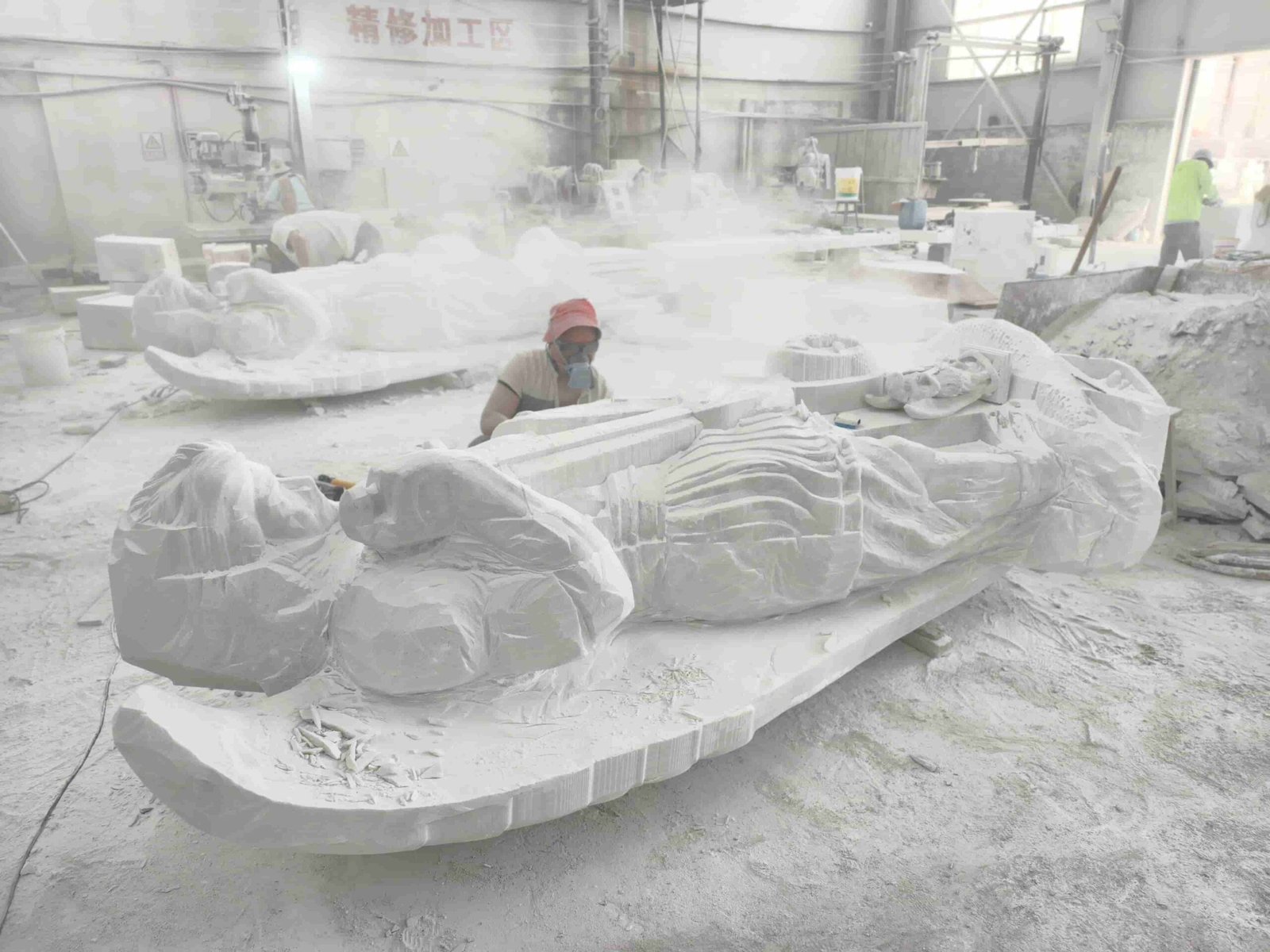 Large Saint Michael statue carving process and details 05 — sculptor inspecting the rough lying blank in the dusty workshop