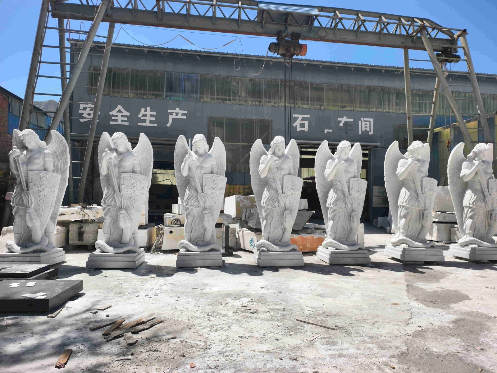 Large Saint Michael statue carving process and details 12 — a row of seven finished Saint Michael statues lined up in the stone-carving workshop yard